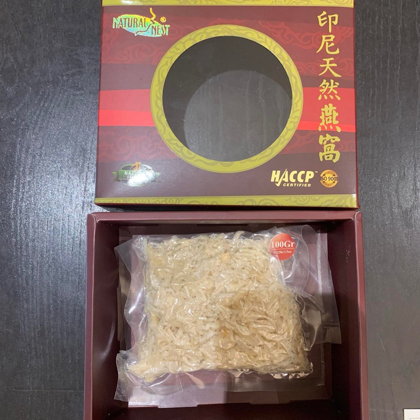 A vacuum-sealed pack of dried bird's nest labeled "Birdnest Premium White Small Broken Bird’s Nest, 100g" inside a red rectangular gift box, available to buy at MyAllures. The box is placed on a dark surface.