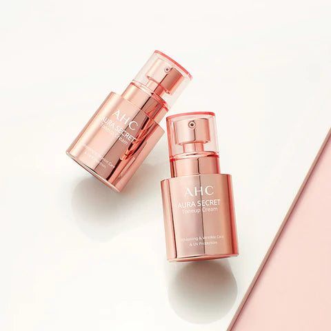 A pink bottle of AHC Aura Secret Tone Up Cream SPF30 PA++ by AHC is placed on a light pink background. The bottle features a pump dispenser and is labeled "Glowing & Moisturizing." You can purchase it at MyAllures.