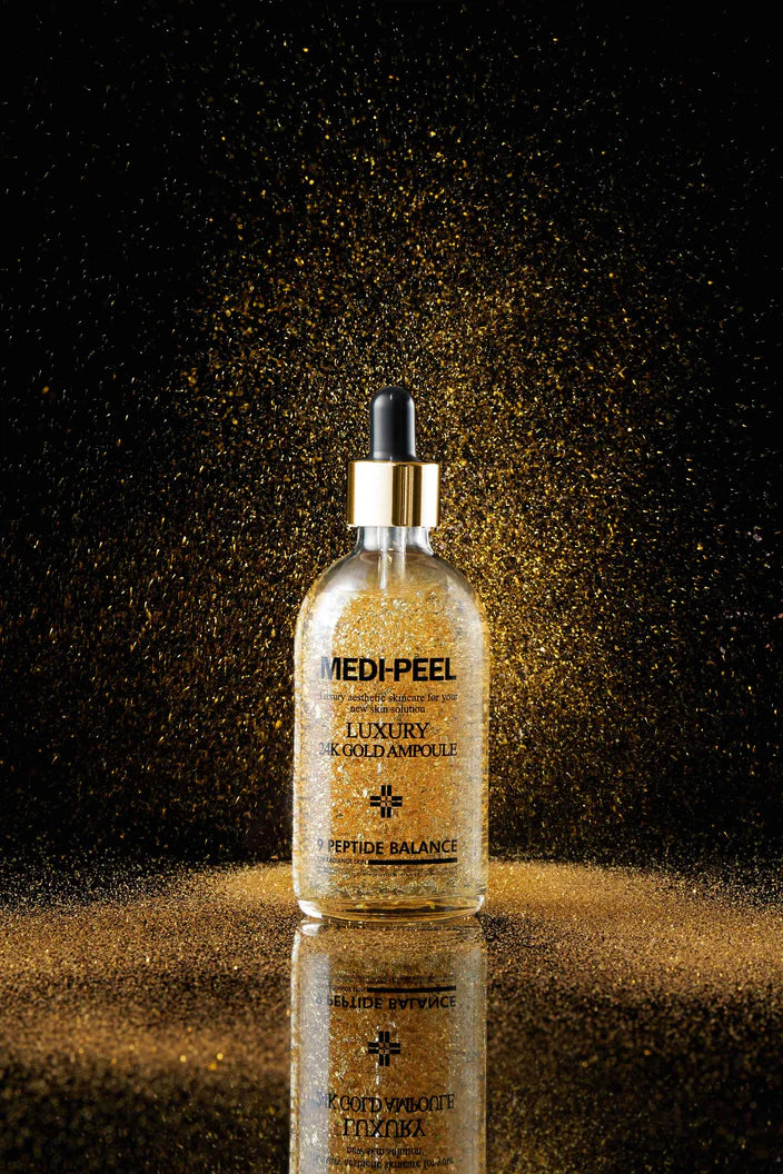 A person uses a dropper to apply the MEDIPEEL LUXURY 24K GOLD AMPOULE serum from a MEDIPEEL bottle to their face, which is available for purchase at MyAllures.