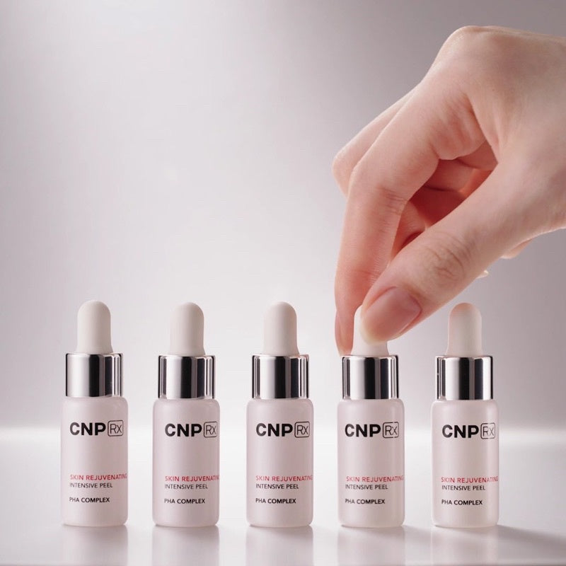 A hand is picking up one of the five dropper bottles labeled "CNP LABORATORY RX Skin Rejuvenating Intensive Peel" with "PHA Complex," available to buy at MyAllures.