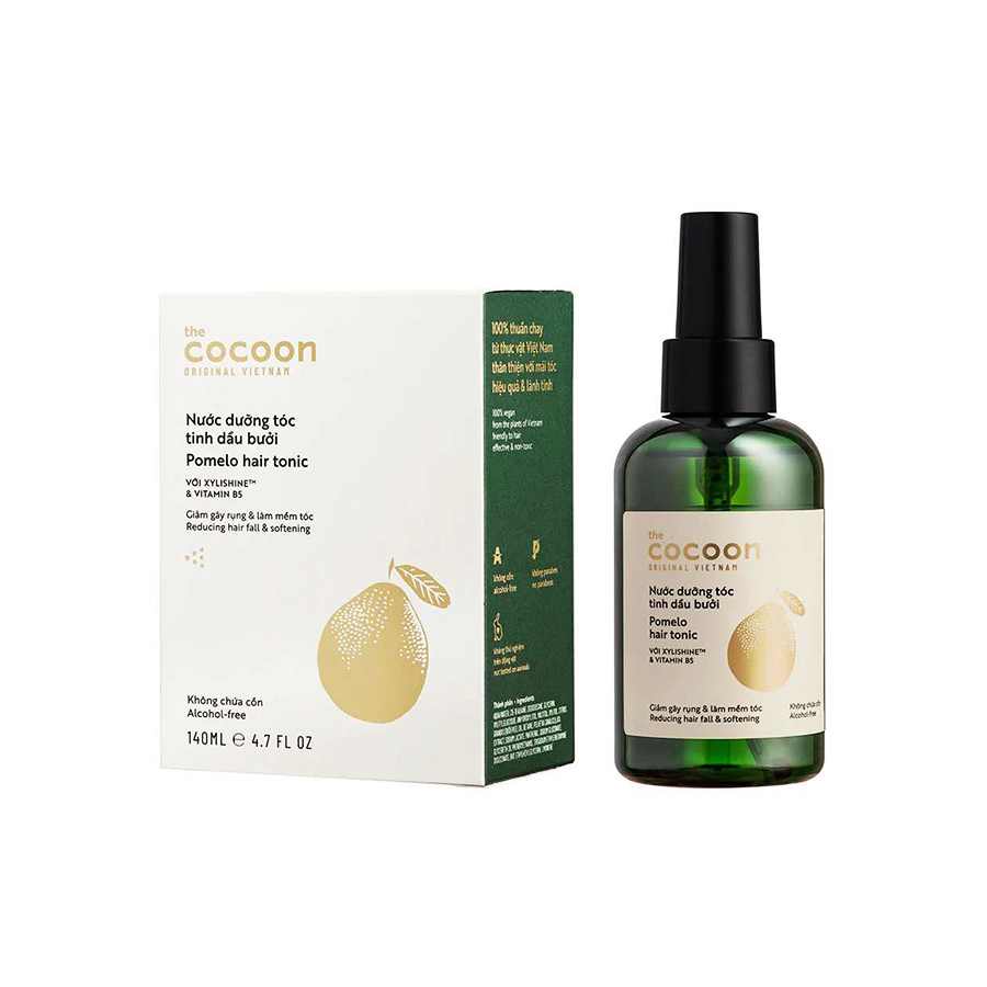 A bottle of COCOON POMELO TONIC HAIR LOSS SOLUTION is surrounded by green leaves and citrus peels, available to buy at MyAllures.