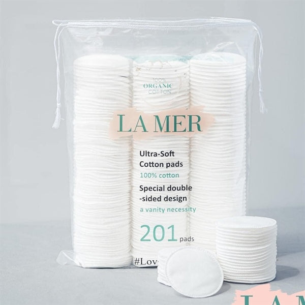 Close-up image of a stack of round, white LAMER cotton pads with one pad in front, partially blurred packaging in the background displaying the text "Special double sided design" and "201 pcs." Buy at MyAllures.