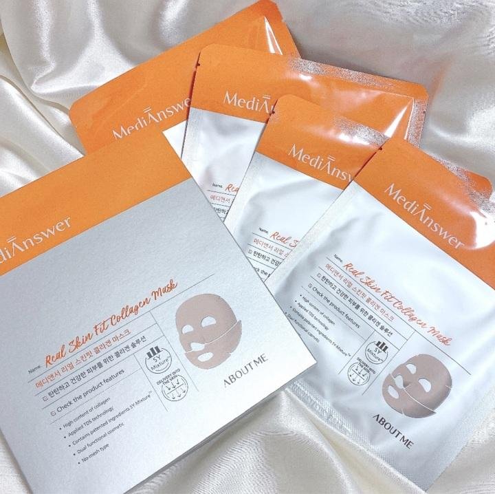 A box of MEDIANSWER REAL FIT COLLAGEN MASK is displayed in front of two glass flasks containing orange liquid. The product packaging is white with orange accents and features text in English and Korean. Purchase this skincare essential at MyAllures for a rejuvenating experience.